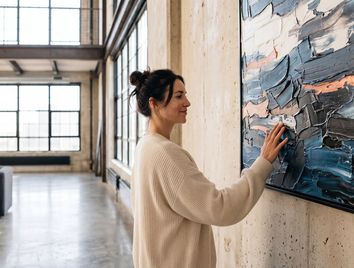Woman admiring a hand painted blue and copper impasto canvas on a concrete wall in a modern loft