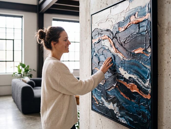 Woman admiring a hand painted blue and copper impasto canvas on a concrete wall in a modern loft